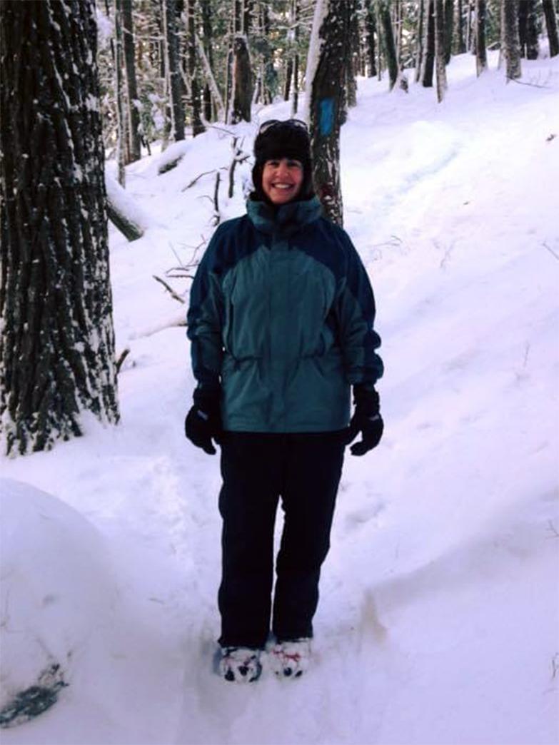 A photo of a woman dressed for the winter and hiking in the woods.